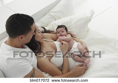 Stock Image - Hispanic family relaxing in bed. Fotosearch
