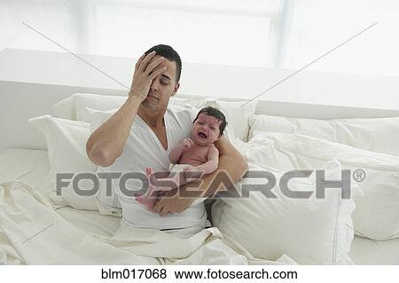 Stock Photo - Hispanic father holding crying baby in bed. Fotosearch