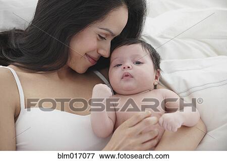 Stock Photo - Hispanic mother holding baby in bed. Fotosearch