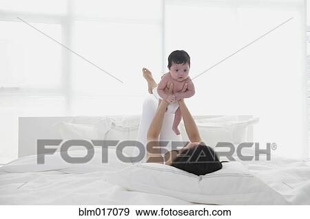 Stock Photo - Hispanic mother playing with baby in bed. Fotosearch