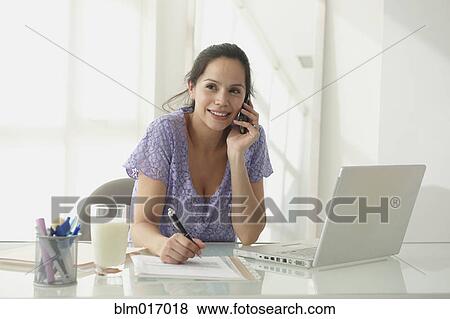 Stock Photo - Hispanic woman talking on cell phone at desk. Fotosearch