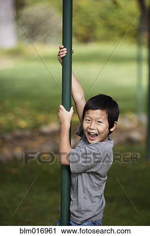 Stock Image - Korean boy climbing pole outdoors. Fotosearch