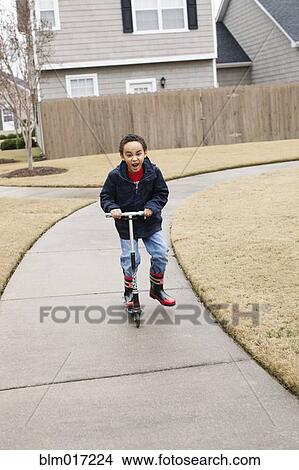 Mixed race boy playing on scooter on suburban street View Large Photo Image Picture - Mixed race boy playing on scooter on suburban street. Fotosearch