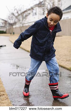 Stock Photo - Mixed race boy splashing in rainboots. Fotosearch