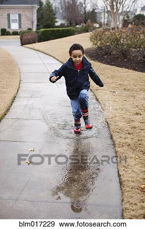 Stock Photo - Mixed race boy splashing in rainboots. Fotosearch