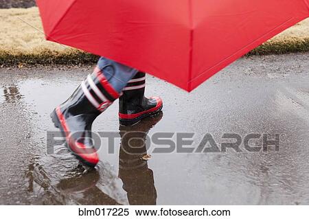Stock Photography - Mixed race boy splashing in rainboots. Fotosearch