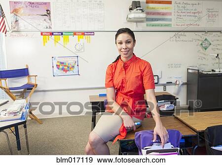 Stock Photo - Mixed race teacher sitting on desk in classroom. Fotosearch