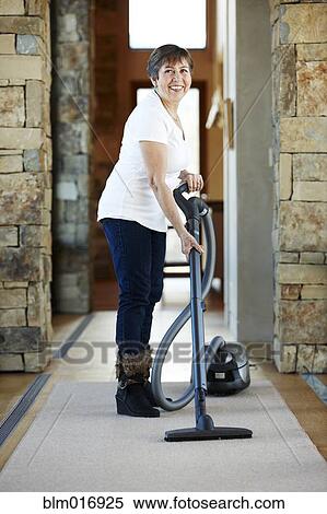 Stock Photography - Older Hispanic woman vacuuming carpet. Fotosearch