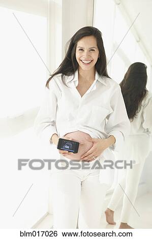 Stock Photograph - Pregnant Hispanic woman holding cell phone. Fotosearch