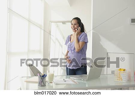 Stock Image - Pregnant Hispanic woman talking on cell phone. Fotosearch