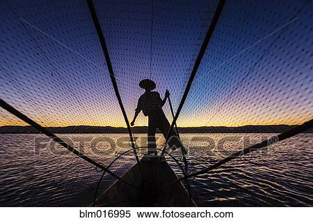 Silhouette of fisherman rowing canoe on water View Large Photo Image Stock Photography - Silhouette of fisherman rowing canoe on water. Fotosearch