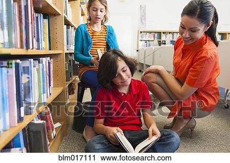Stock Image - Students and teacher reading in library. Fotosearch