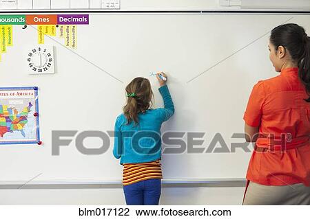 Teacher watching student write on whiteboard in classroom View Large Photo Image Stock Image - Teacher watching student write on whiteboard in classroom. Fotosearch