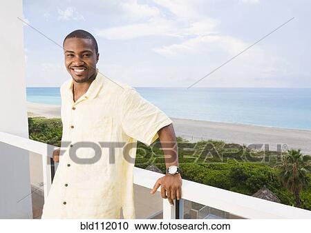Stock Image - African American man standing on balcony. Fotosearch