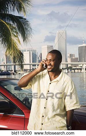 Stock Image - African American man talking on cell phone by car. Fotosearch
