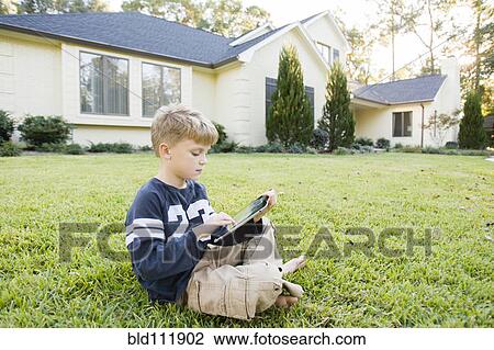 Caucasian boy using digital tablet on lawn View Large Photo Image Stock Image - Caucasian boy using digital tablet on lawn. Fotosearch