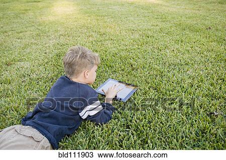 Caucasian boy using digital tablet on lawn View Large Photo Image Stock Image - Caucasian boy using digital tablet on lawn. Fotosearch
