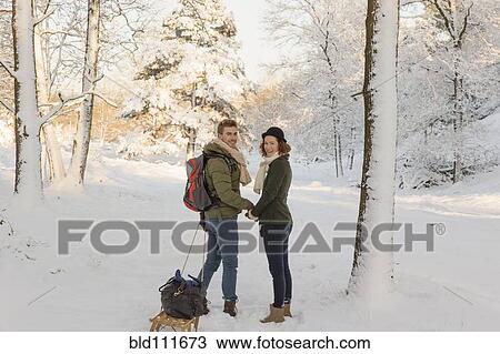 Stock Image - Caucasian couple pulling sled in snow. Fotosearch