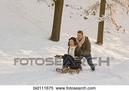 Stock Photography - Caucasian man pushing girlfriend on sled in snow. Fotosearch