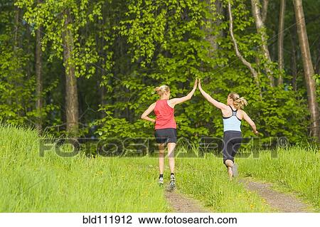 Stock Image - Caucasian runners high fiving on path. Fotosearch