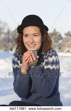 Stock Image - Caucasian woman drinking coffee in snow. Fotosearch