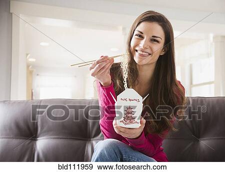 Stock Photo - Caucasian woman eating Chinese food on sofa. Fotosearch
