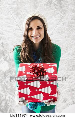 Picture - Caucasian woman holding Christmas gift in snow. Fotosearch