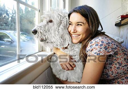 Stock Photography - Caucasian woman hugging dog at window. Fotosearch