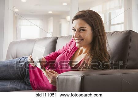Stock Image - Caucasian woman reading papers on sofa. Fotosearch