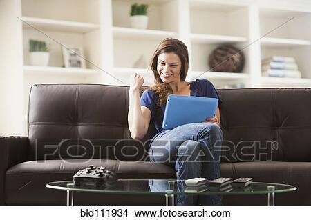 Picture - Caucasian woman using digital tablet on sofa. Fotosearch