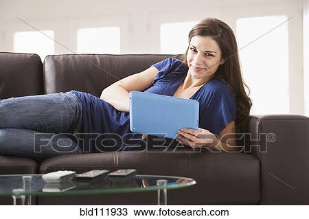Stock Image - Caucasian woman using digital tablet on sofa. Fotosearch