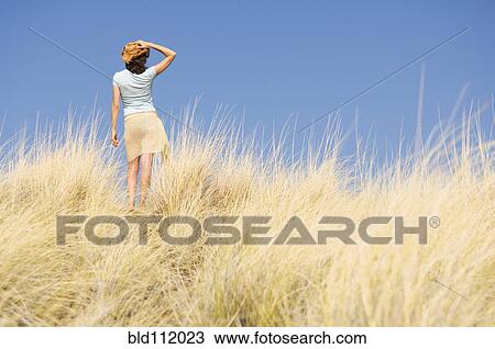 Stock Image - Caucasian woman walking in tall grass. Fotosearch