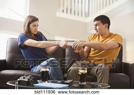 Stock Photograph - Couple arguing over remote on sofa. Fotosearch