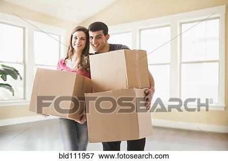 Couple carrying cardboard boxes in new home View Large Photo Image Stock Photo - Couple carrying cardboard boxes in new home. Fotosearch