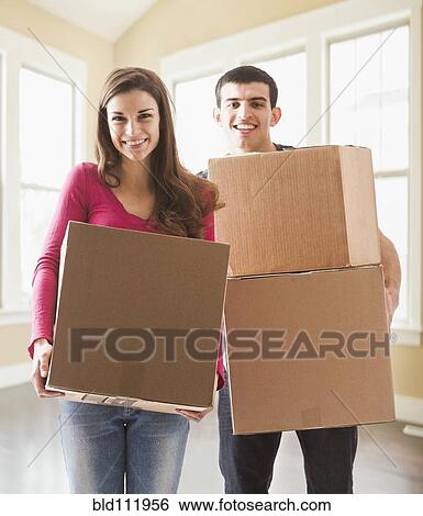 Couple carrying cardboard boxes in new home View Large Photo Image Stock Photograph - Couple carrying cardboard boxes in new home. Fotosearch