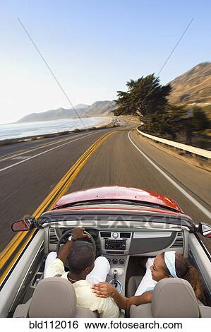 Stock Photograph - Couple driving convertible on coastal road. Fotosearch