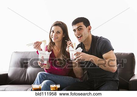 Stock Photo - Couple eating Chinese food on sofa. Fotosearch