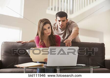 Stock Photograph - Couple reading papers at laptop together. Fotosearch