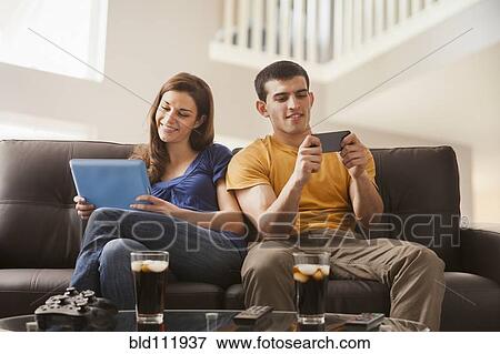 Stock Photo - Couple relaxing with technology on sofa. Fotosearch