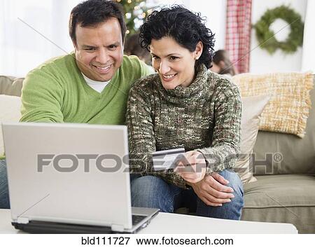 Stock Photo - Couple shopping online in living room. Fotosearch