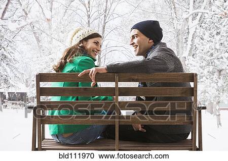 Stock Image - Couple sitting on park bench in snow. Fotosearch
