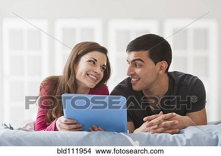 Picture - Couple using digital tablet on bed. Fotosearch