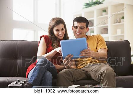 Stock Image - Couple using digital tablet on sofa. Fotosearch