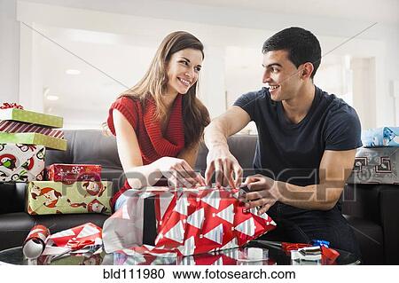 Couple wrapping Christmas presents in living room View Large Photo Image Stock Image - Couple wrapping Christmas presents in living room. Fotosearch