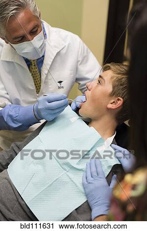 Stock Image - Dentist and nurse examining patient's mouth. Fotosearch