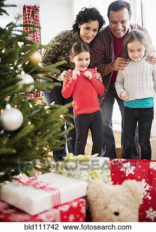 Stock Image - Family examining presents under Christmas tree. Fotosearch
