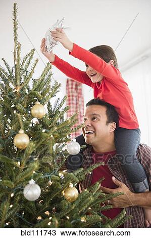 Stock Image - Father and daughter decorating Christmas tree. Fotosearch