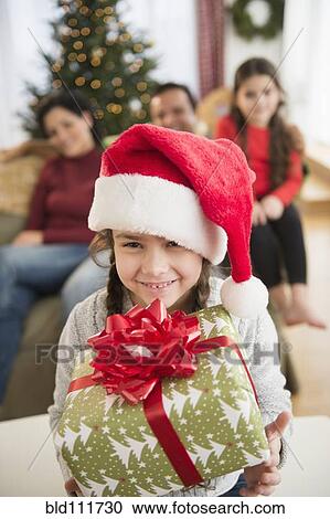 Stock Image - Girl in Santa hat holding Christmas present. Fotosearch