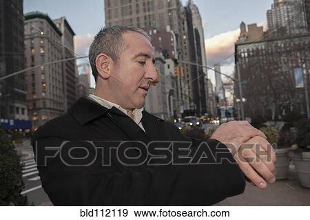 Stock Photo - Hispanic businessman checking watch on city street. Fotosearch