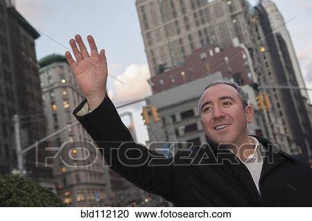 Stock Image - Hispanic businessman hailing taxi on city street. Fotosearch